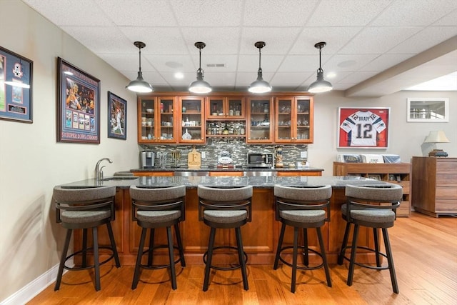 bar with decorative backsplash, wet bar, a sink, stainless steel microwave, and light wood-style floors