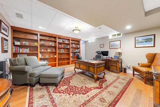 home office with built in features, a drop ceiling, light wood finished floors, and visible vents
