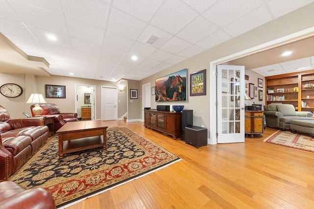 living room with visible vents, built in features, a paneled ceiling, and light wood-style floors