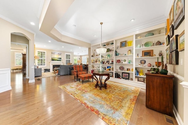 living area featuring crown molding, a fireplace, light wood-type flooring, recessed lighting, and arched walkways