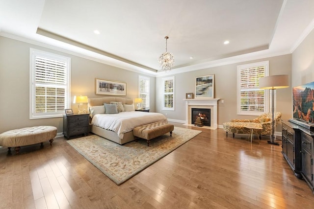 bedroom featuring wood-type flooring, a fireplace with flush hearth, ornamental molding, and a raised ceiling