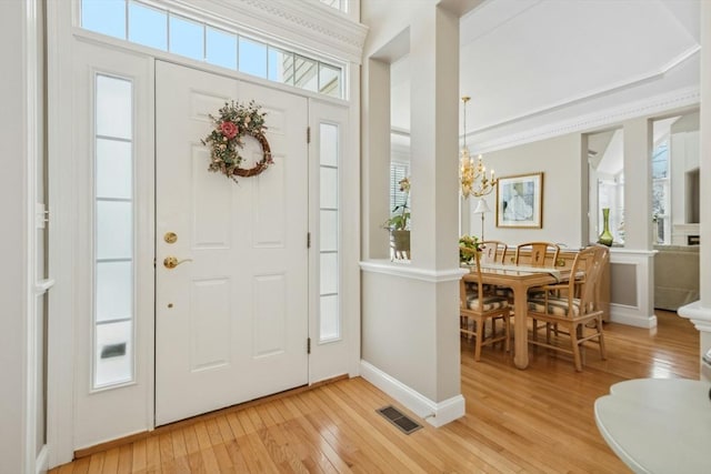 foyer with crown molding, a chandelier, and light wood-type flooring