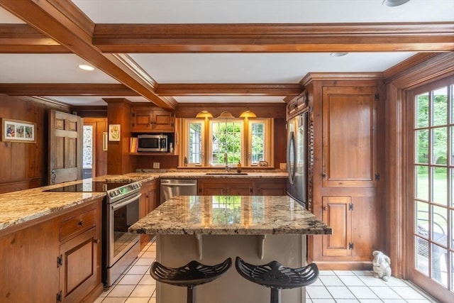 188 Main St, Wilbraham, MA 01095 - kitchen with stainless steel appliances, brown cabinetry, light tile patterned flooring, beamed ceiling, and a kitchen island