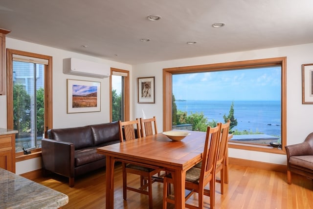 dining room with a wall mounted air conditioner, light hardwood / wood-style floors, and a water view