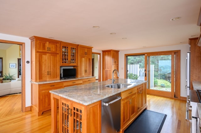 kitchen with light wood-type flooring, light stone countertops, a kitchen island with sink, stainless steel fridge, and sink