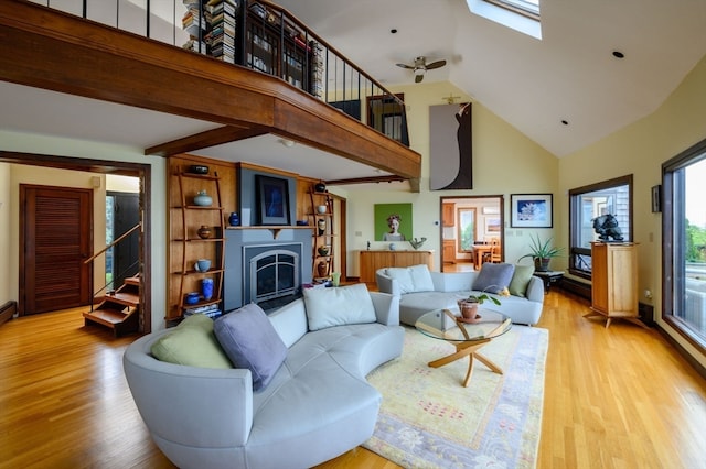 living room featuring high vaulted ceiling, a skylight, light wood-type flooring, and ceiling fan