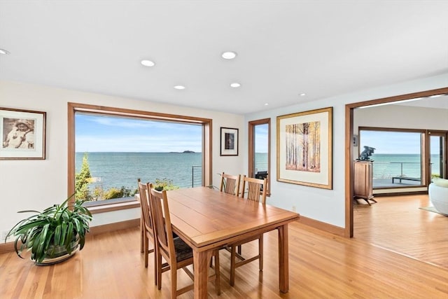 dining space with recessed lighting, baseboards, light wood-style flooring, and a water view