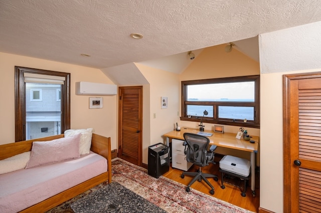 office space with lofted ceiling, light hardwood / wood-style floors, a wall unit AC, and a textured ceiling