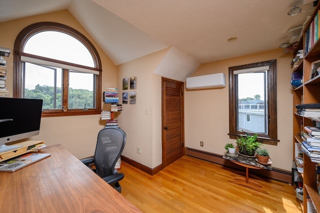 office featuring lofted ceiling, light wood-type flooring, a wall mounted AC, and a wealth of natural light