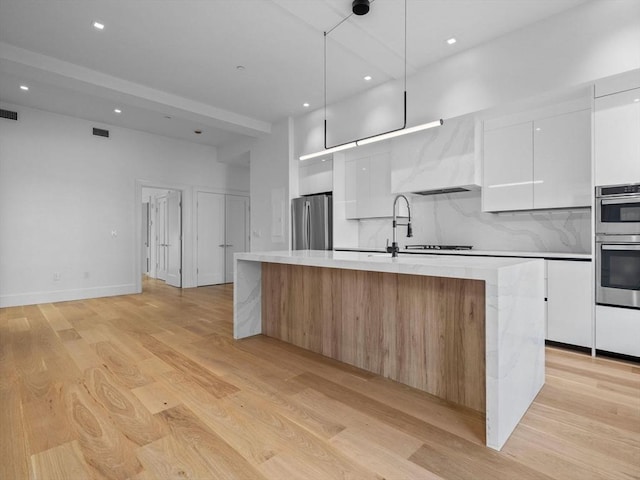 kitchen featuring white cabinetry, appliances with stainless steel finishes, light wood-type flooring, modern cabinets, and a large island with sink