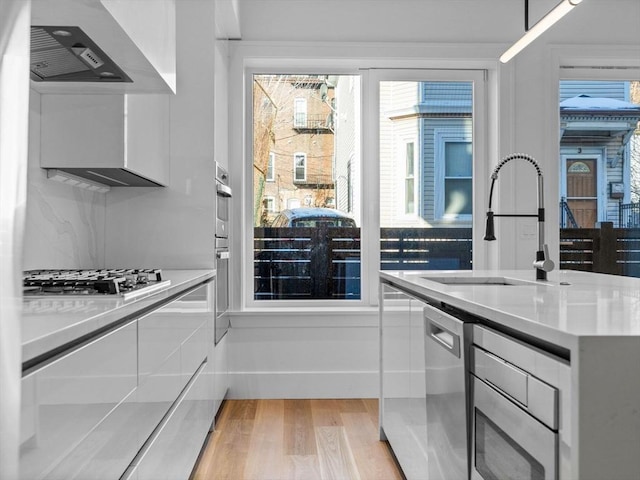 kitchen with stainless steel appliances, light countertops, light wood-style flooring, white cabinetry, and a sink