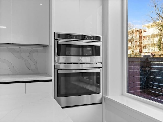 kitchen featuring tasteful backsplash, double oven, light stone counters, and white cabinets