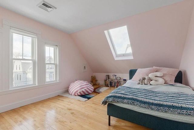 bedroom featuring visible vents, lofted ceiling with skylight, baseboards, and wood finished floors