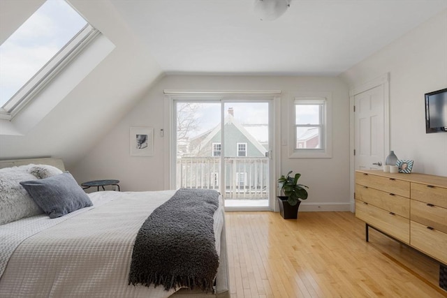 bedroom with access to exterior, lofted ceiling with skylight, baseboards, and light wood-style floors