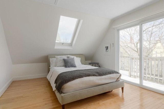 bedroom featuring light wood-type flooring, lofted ceiling with skylight, baseboards, and access to outside