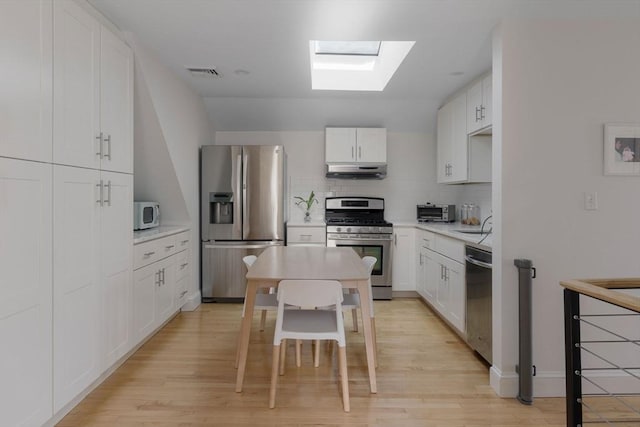 kitchen featuring under cabinet range hood, appliances with stainless steel finishes, a skylight, light countertops, and decorative backsplash