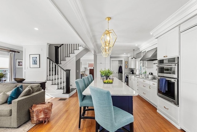 kitchen featuring double oven, wall chimney range hood, hanging light fixtures, and white cabinets