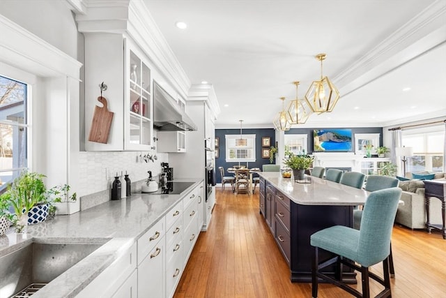 kitchen with a kitchen bar, ornamental molding, pendant lighting, light stone countertops, and white cabinets