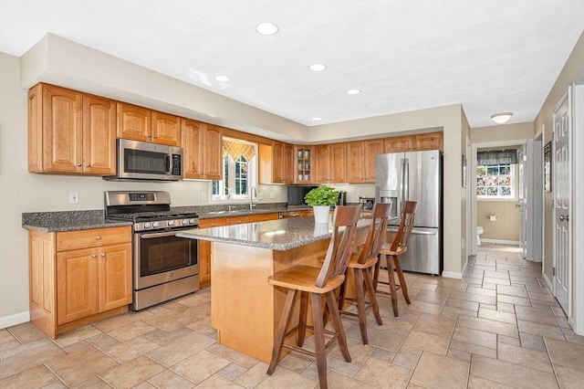 kitchen with appliances with stainless steel finishes, baseboards, dark stone counters, a kitchen breakfast bar, and recessed lighting
