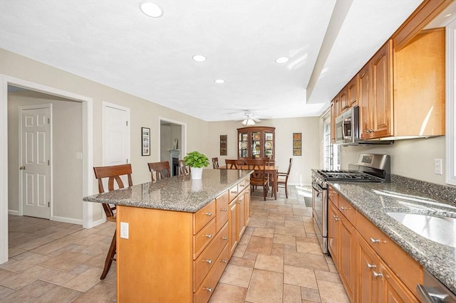 kitchen with appliances with stainless steel finishes, a breakfast bar area, stone tile floors, recessed lighting, and a center island