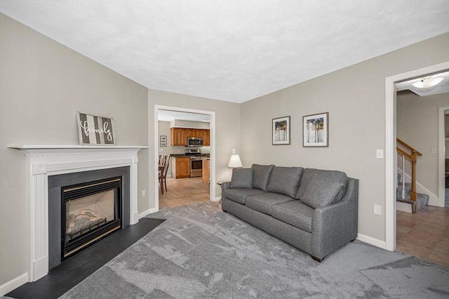 living room with stairway, a glass covered fireplace, and baseboards