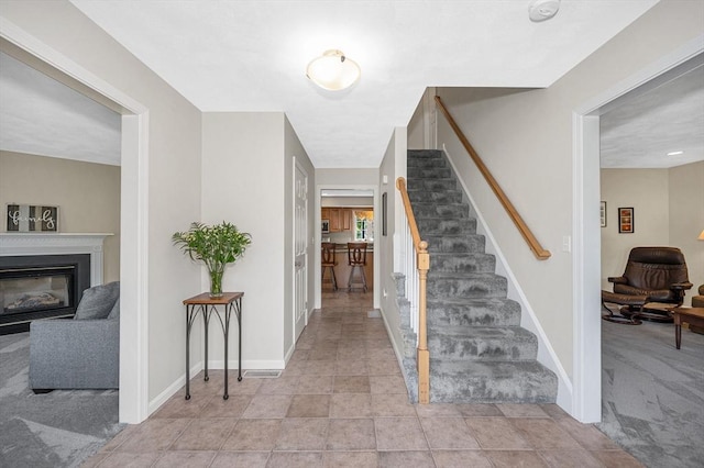stairs with carpet floors, a glass covered fireplace, and baseboards