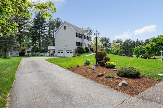 view of front facade with an attached garage, a front yard, driveway, and view of wooded area