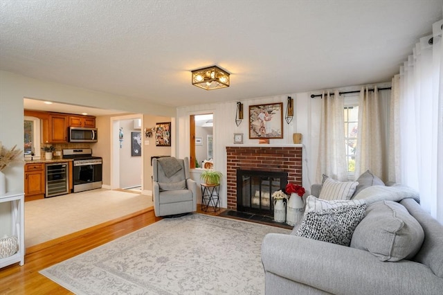 living room with wine cooler, a fireplace, a textured ceiling, and light wood-type flooring