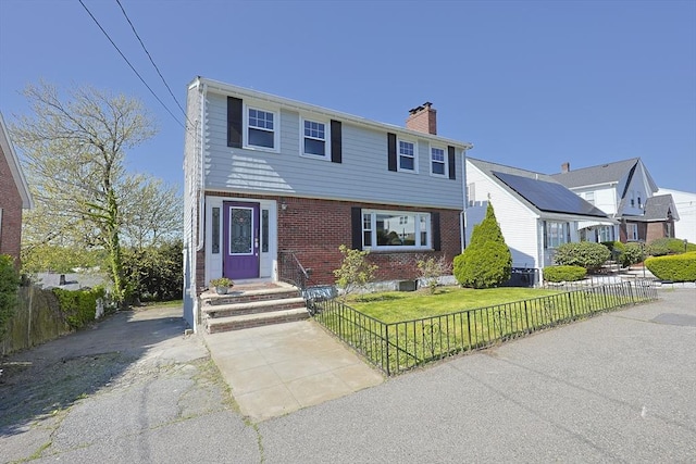 colonial house featuring a chimney, brick siding, and entry steps