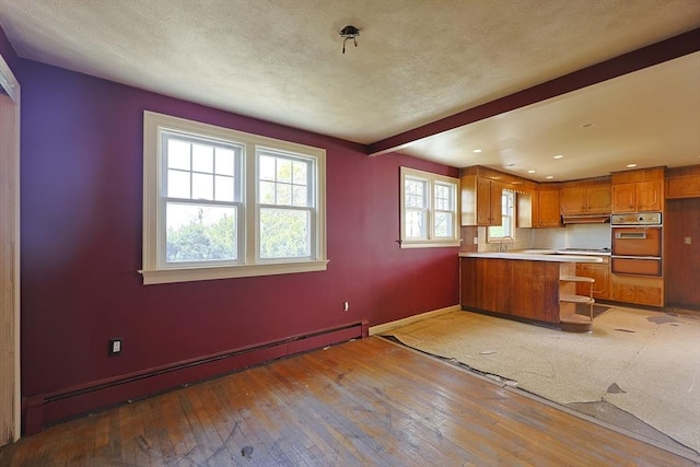 kitchen featuring a baseboard heating unit, a warming drawer, wall oven, brown cabinetry, and a peninsula
