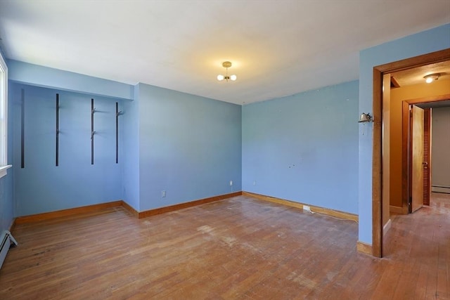 unfurnished bedroom with wood-type flooring, baseboards, and a baseboard heating unit
