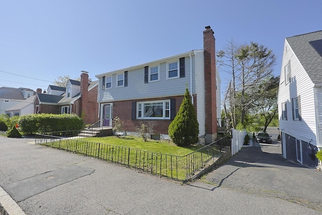 colonial-style house with brick siding, a chimney, and driveway