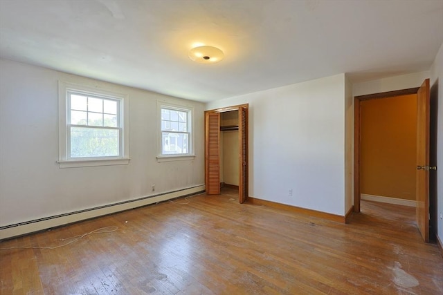 unfurnished bedroom featuring baseboard heating, hardwood / wood-style floors, a closet, and baseboards