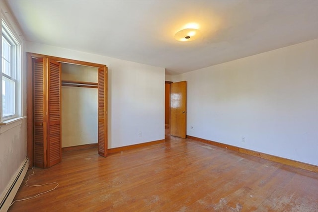 unfurnished bedroom with a baseboard heating unit, a closet, wood finished floors, and multiple windows