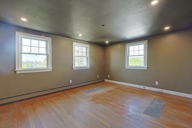 empty room with a baseboard heating unit, wood finished floors, baseboards, and recessed lighting