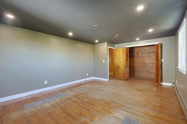 unfurnished bedroom with a baseboard heating unit, baseboards, a closet, recessed lighting, and light wood finished floors