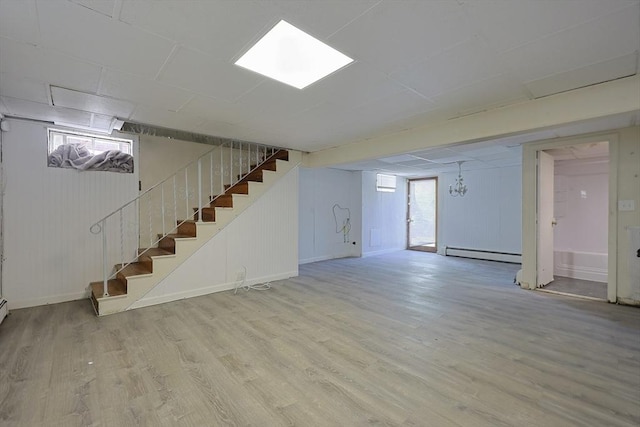 basement with a baseboard heating unit, stairway, wood finished floors, and baseboards