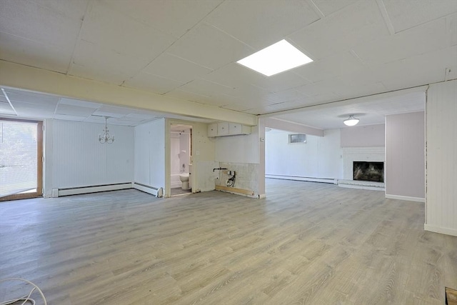 basement with a baseboard heating unit, a fireplace with raised hearth, a baseboard radiator, light wood finished floors, and a chandelier