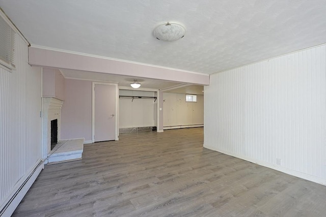 unfurnished living room with a baseboard heating unit, wood finished floors, a fireplace with raised hearth, and baseboards