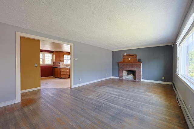 unfurnished living room with a textured ceiling, wood finished floors, a baseboard heating unit, healthy amount of natural light, and a fireplace