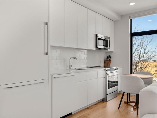 kitchen with decorative backsplash, a sink, light countertops, light wood-style floors, and stainless steel appliances