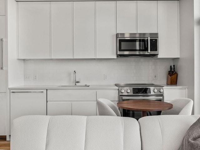 kitchen with tasteful backsplash, light countertops, a sink, white cabinets, and stainless steel appliances