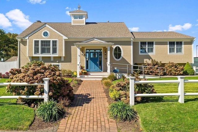 view of front facade with a shingled roof, fence, and a front yard