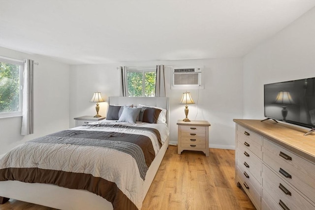 bedroom with light wood finished floors, a wall mounted air conditioner, and baseboards