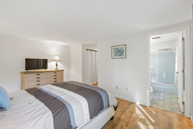 bedroom with light wood-style floors, baseboards, visible vents, and ensuite bath