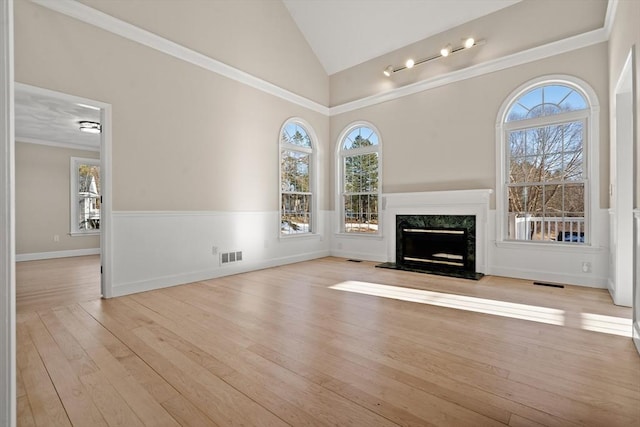 unfurnished living room featuring a premium fireplace, plenty of natural light, ornamental molding, and light wood-type flooring