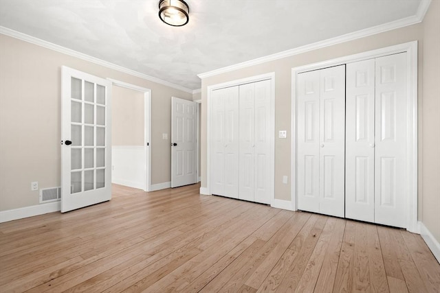 unfurnished bedroom featuring crown molding, two closets, and light wood-type flooring