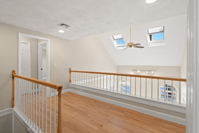 corridor with hardwood / wood-style flooring and vaulted ceiling with skylight