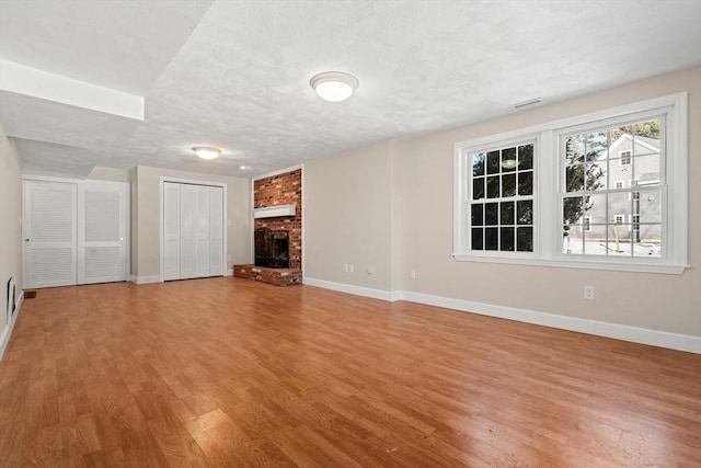 unfurnished living room with a brick fireplace, a textured ceiling, and light wood-type flooring