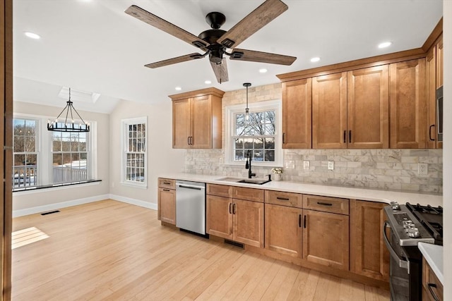 kitchen featuring sink, gas range, decorative light fixtures, light wood-type flooring, and dishwasher